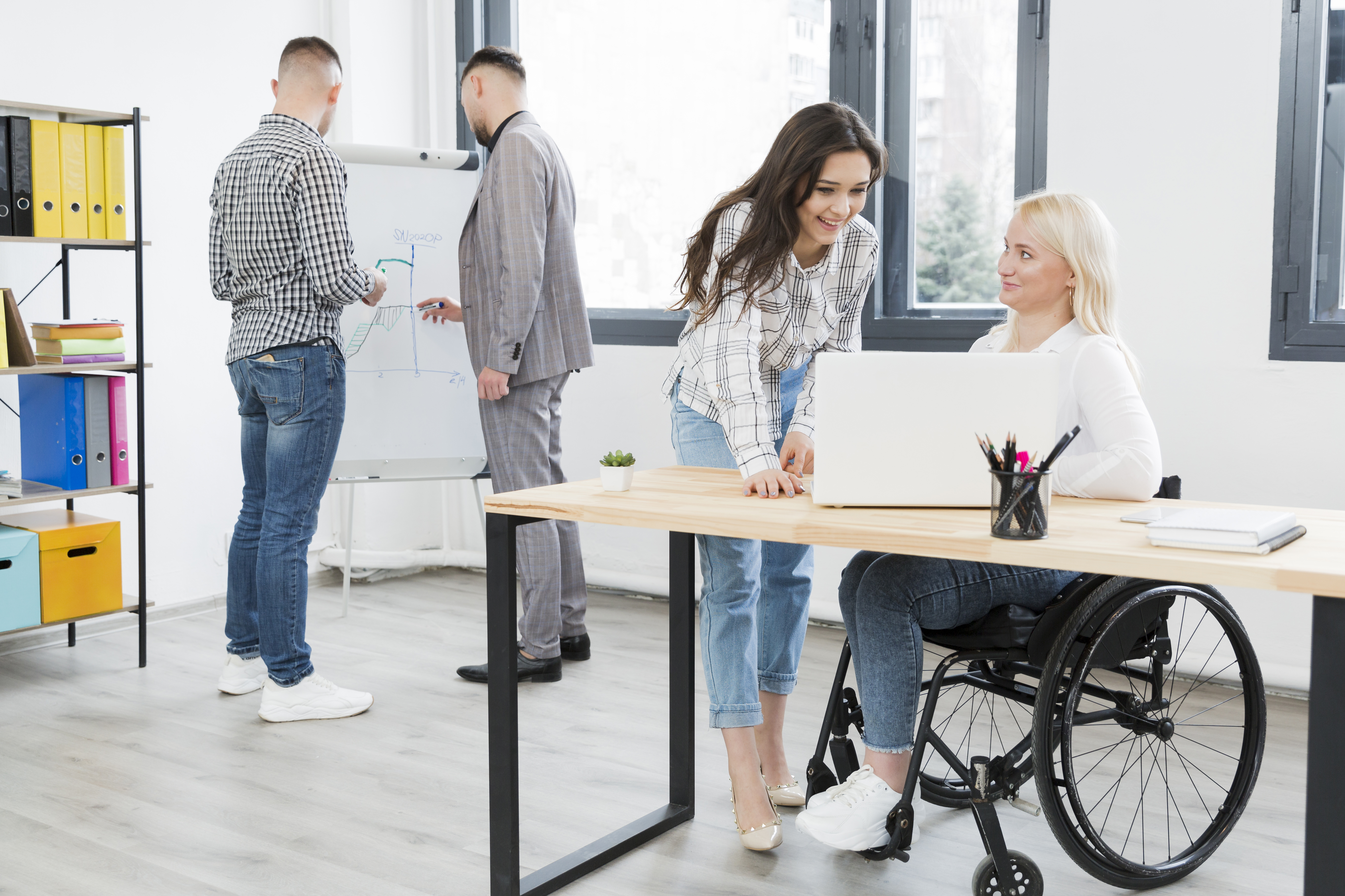 Dos hombres y dos mujeres trabajando en una oficina. Una de las mujeres está en silla de ruedas.